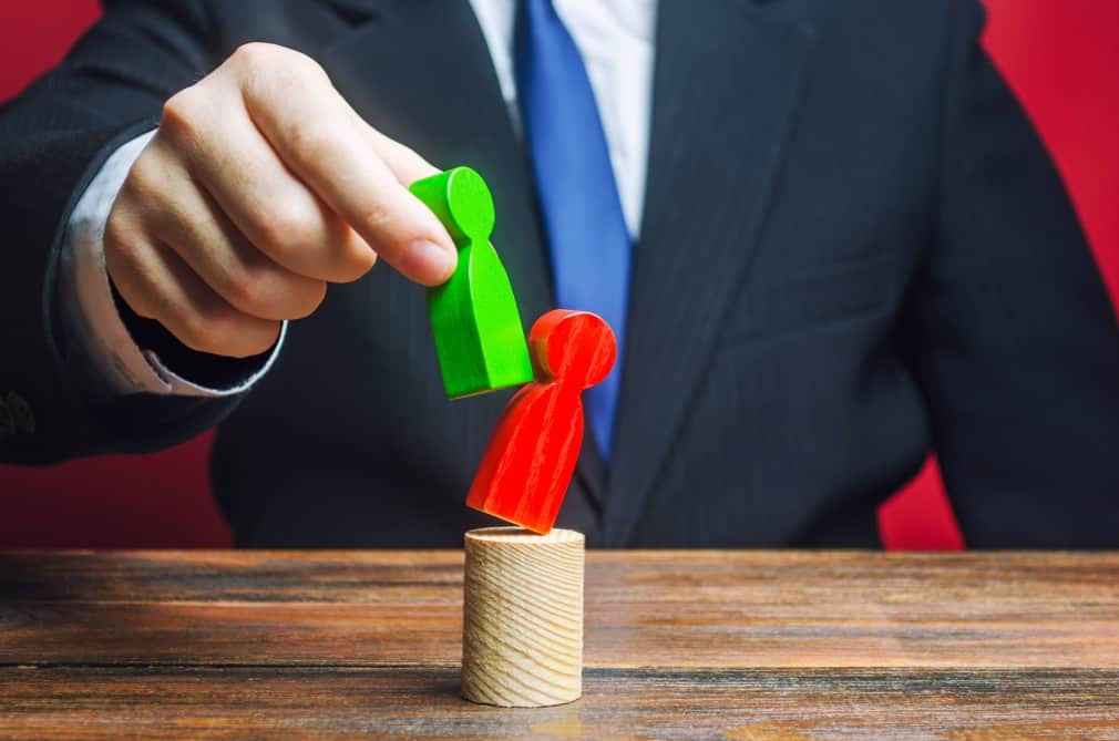 Man using green wooden figure to knock red wooden figure over